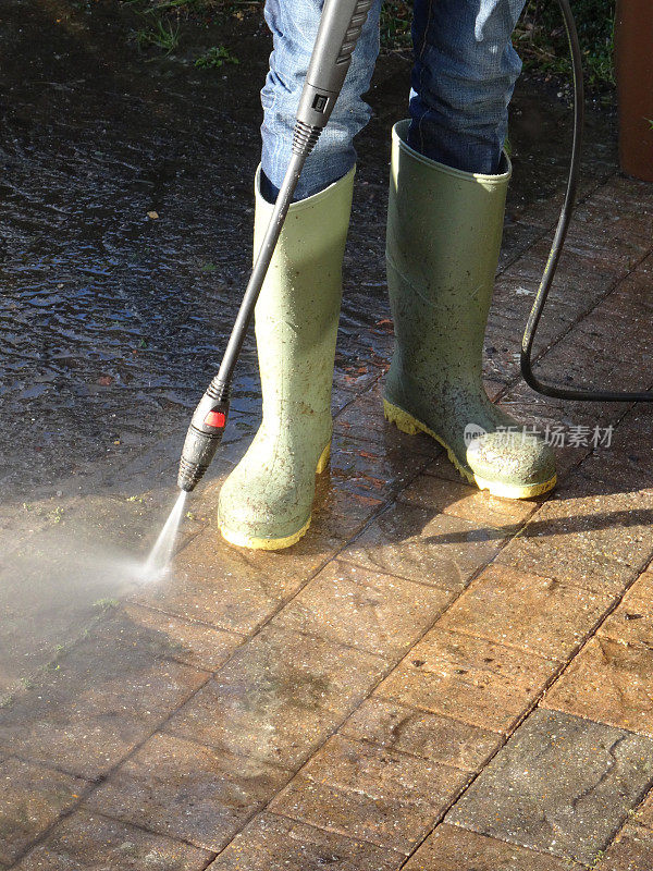 男孩穿着雨靴软管/压力清洗砖驱动器与动力洗衣机的图像